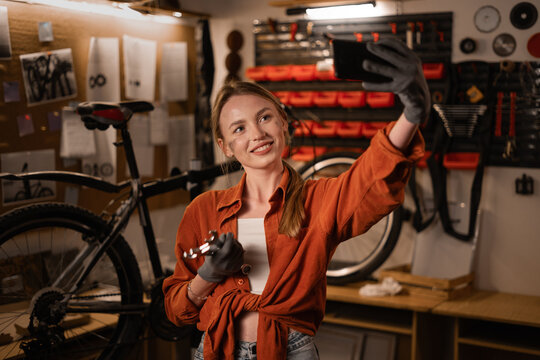 Young female Mechanic in a workshop takes a selfie after finished working on a repair bicycle