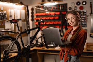 Female mechanic in her Workshop or garage looking at laptop. Bike shop owner with laptop
