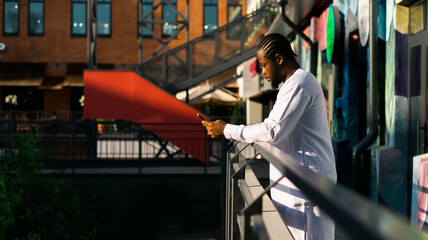 Millennial generation african american man typing sms outdoor 5g internet concept. High speed...