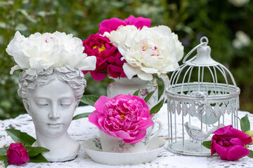 florales Arrangement mit pink und weißen Pfingstrosen, Frauenbüste und vintage Vogelkäfig 