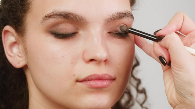 Eye shadow makeup to the upper eyelid, close-up. Makeup artist applies a bright eye shadow with a make-up brush.Tutorial master class of professional makeup, smoky eyes 