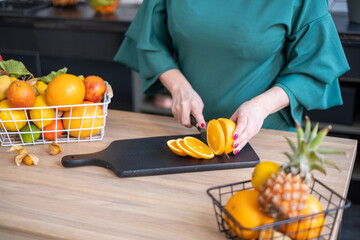  A chef in a teal blouse slices fresh oranges on a black cutting board, with a basket of vibrant...