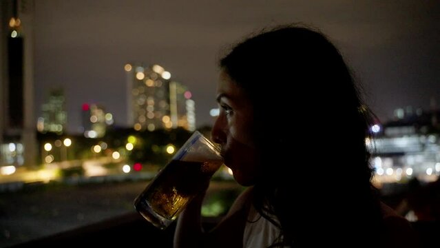 Woman drinking beer with city skyline in the background night