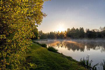 Fog illuminated by rays of rising sun over ponds