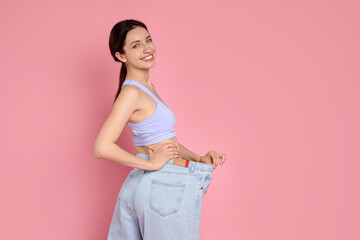 Happy young woman in big jeans showing her slim body on pink background, space for text
