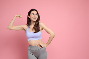 Naklejka premium Happy young woman with slim body showing her muscles on pink background, space for text
