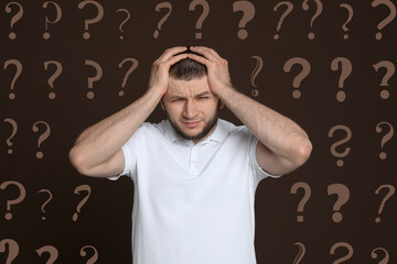 Amnesia. Confused man and question marks on brown background