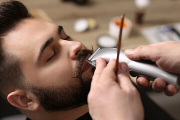 Professional barber trimming client's mustache in barbershop, closeup