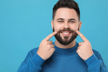 Happy young man touching mustache on light blue background