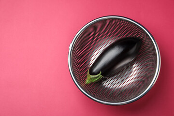 Colander with fresh eggplant on pink table, top view. Space for text