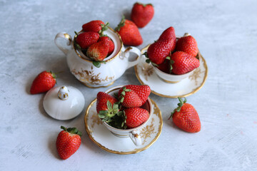 Strawberries in porcelain cups on a white background. Light grey textured background with space for text. Ripe summer berries close up photo. Healthy eating concept. 