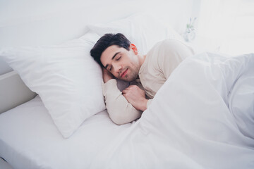 Photo of young attractive man enjoying sleepwear lying in soft comfy bed white room interior inside