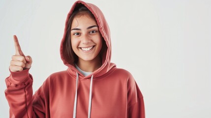 Cheerful young woman in a red hoodie pointing up with a bright smile against a white background. - Powered by Adobe
