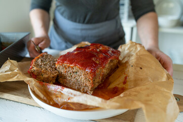 Person with fresh sliced whole meatloaf with ketchup glaze
