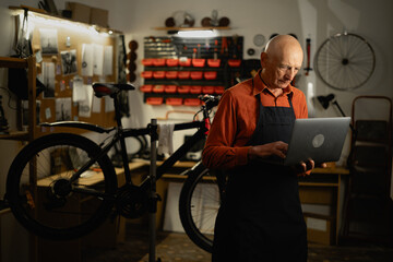 Bicycle repair shop owner, old mechanic with laptop working in his garage