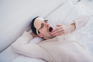 Photo of sleepy tired young man lying in soft comfortable bed want sleep white room interior inside
