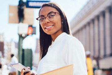 Portrait of prosperous african american businesswoman in white shirt strolling in downtown with...