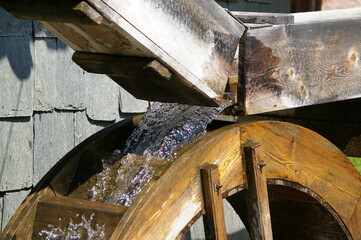 Fresh cold clear water running over a wooden waterwheel in the bright sunlight. 