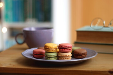 Purple plate filled with pastel macarons, cup of tea or coffee, vintage books and reading glasses...