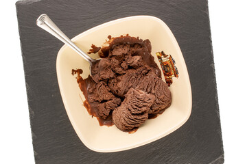 Chocolate ice cream in a ceramic bowl with a spoon on a slate stone, macro, top view.