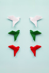 Two groups three paper origami pigeons white, green and red on light background facing each other