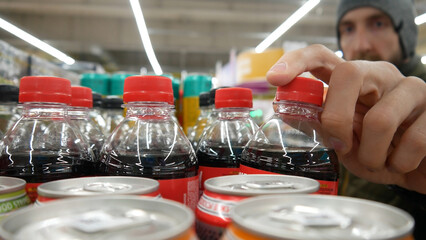 Close-up of a male buyer's hand taking a plastic bottle of cola from a supermarket shelf
