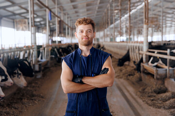 Portrait young man farmer or vet doctor on background cows in cowshed on dairy farm. Agriculture...