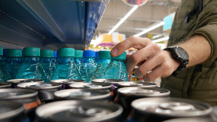 Close-up of a male bayer's hand taking a plastic bottle of mineral water from a supermarket shelf