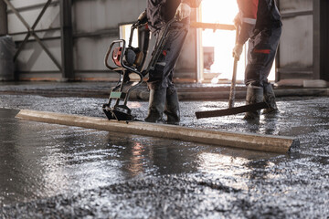 Team Workers uses vibrating machine to level cement mortar for floors. Concrete screed for...