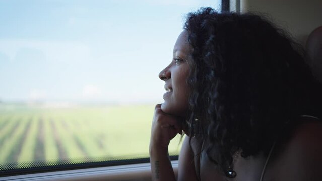 Young African girl traveling by train, looking out the window admiring the scenery and deep in thought. Footage with copy space.