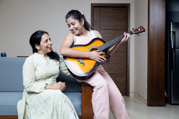 Young Teen Girl with Mother and home playing Guitar and mother enjoying the moment at home sitting...