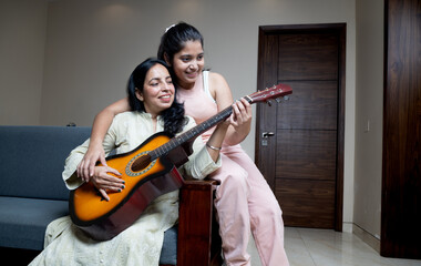 Indian Young Teenage Daughter Helping mother with Guitar Playing at home sitting on sofa, Mother...