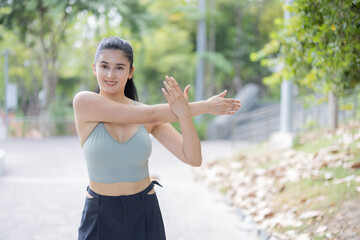 Sport woman warming up by stretching her shoulder in a park