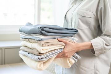 Feel softness, chore of asian young woman, girl housewife hand holding pile clothing from table,...