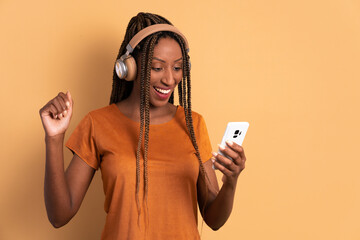 happy black young woman listening to music with headphones in beige colors. app, social media, addiction, network concept.