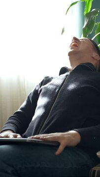 A tearful man, laptop in hand, expresses furious anguish indoors. Emotional, raw gestures webcore style. Gripping portrayal of agony Vertical footage.