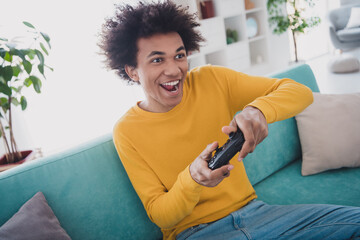 Photo of glad cheerful man sitting divan playing game enjoying vacation living room indoors