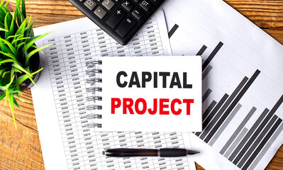 CAPITAL PROJECT text on notebook on chart with calculator and pen