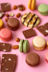 Pastel macarons, almond chocolate, peanut butter cookies and various nuts on bright pink background. Selective focus.