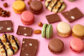 Pastel macarons, almond chocolate, peanut butter cookies and various nuts on bright pink background. Selective focus.