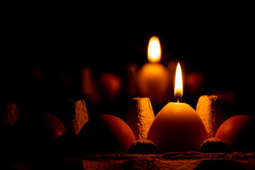 A yellow candle in the shape of an egg in the dark on a tray with chicken eggs stands near a...
