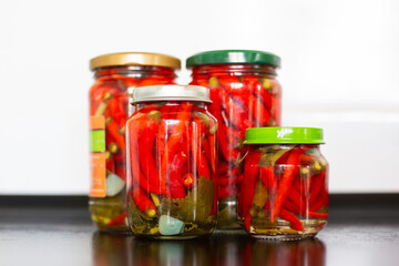 Pickled red hot hot chili peppers in jars on a black table. Canning vegetables