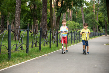 Two attractive European boys brothers, wearing red and white checkered shirts, standing on scooters...