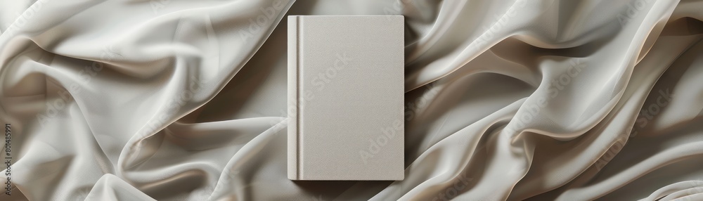 Poster A book is on a white cloth. The cloth is folded and has a pattern. The book is placed on the cloth in a way that it is the center of attention