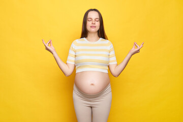 Calm relaxed Caucasian pregnant woman with bare belly wearing casual top isolated over yellow...