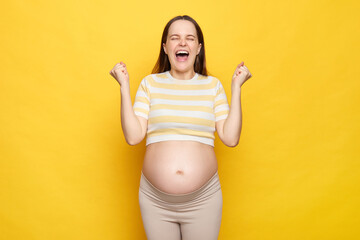 Extremely happy overjoyed Caucasian pregnant woman with bare belly wearing casual top isolated over...