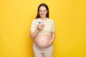 Overjoyed Caucasian pregnant woman with bare belly wearing casual top isolated over yellow...