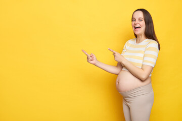 Amazed Caucasian pregnant woman with bare belly wearing casual top isolated over yellow background...