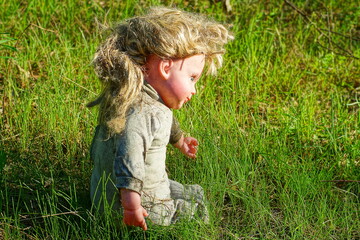 
an old, dirty, torn children's toy small in gray clothes with a plastic face and hair, a girl's doll lies on the green grass  during the day on the street
