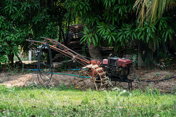 walking tractor rotativo used to pump water to Banana tree plantation,Coconut Garden integrated agriculture nature the garden with daylight blue sky white clouds in Thailand.